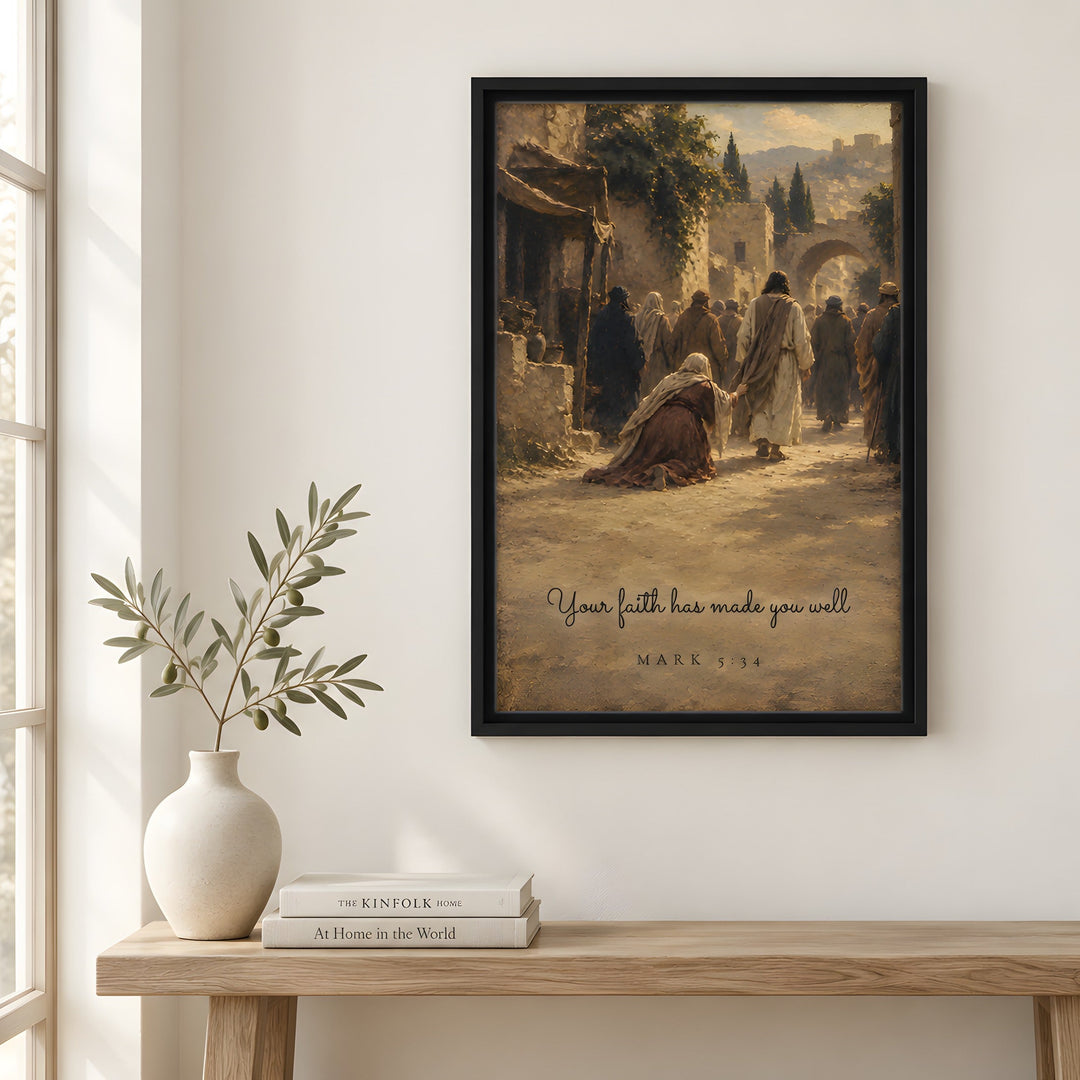 A framed art print featuring a vintage-style illustration of biblical figures in a street scene with the quote 'Your faith has made you weak' and 'MARK 1:24' at the bottom, displayed on a white wall above a wooden console table with a vase and books.