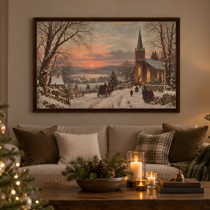 A framed winter landscape painting hangs on a beige wall above a sofa in a cozy living room. The artwork depicts a snowy village street with a church, bare trees, and a warm sunset sky.