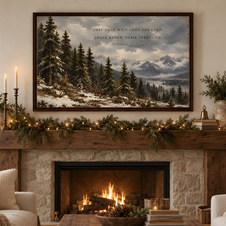 A framed landscape art print depicting a snowy pine forest and mountains with a scripture quote, displayed above a rustic stone fireplace with a burning fire, green garlands, and warm holiday lights in a cozy living room setting.