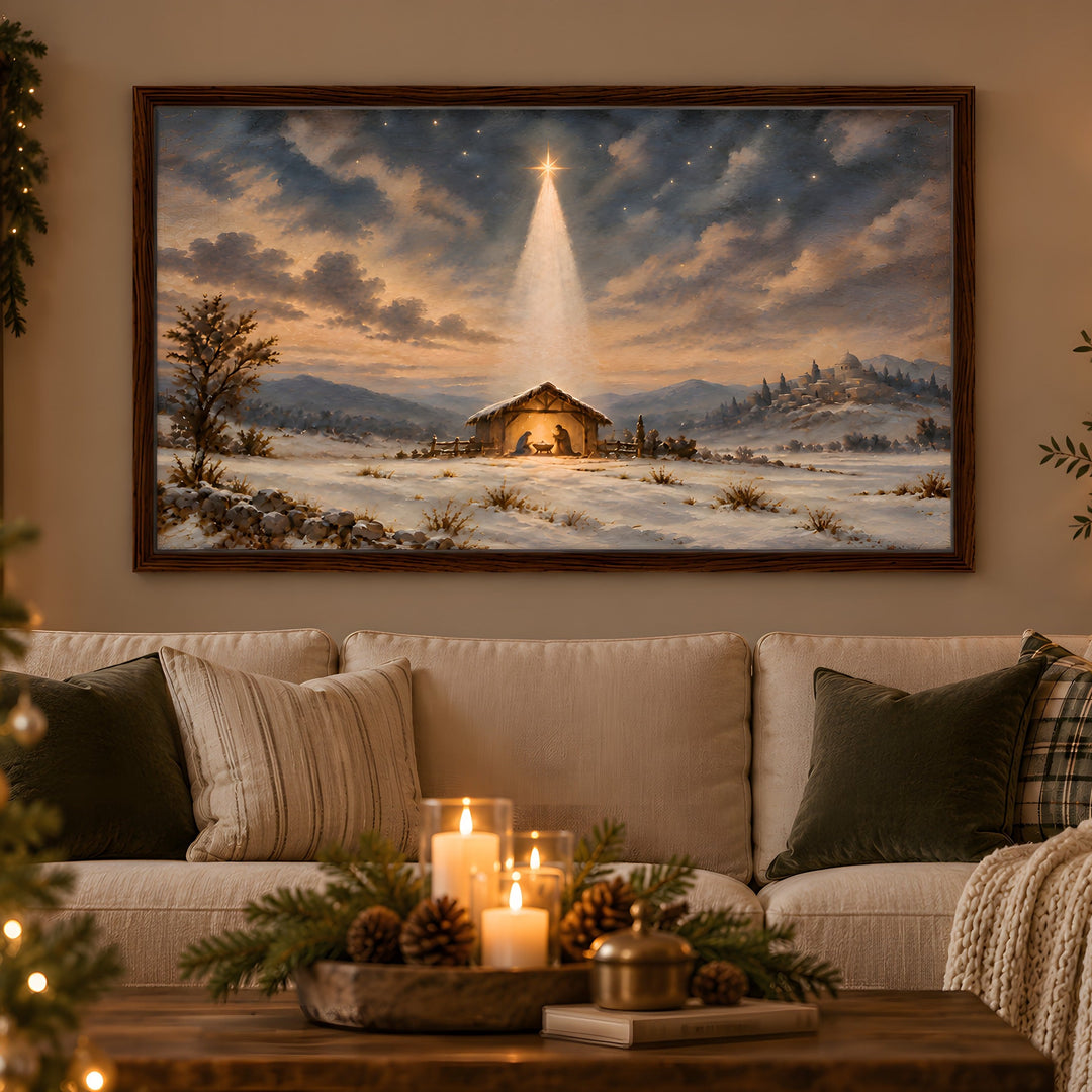 A framed Christmas landscape painting hangs above a stone fireplace in a cozy living room. The painting depicts a snowy winter scene with a small stable under a glowing star in the night sky.