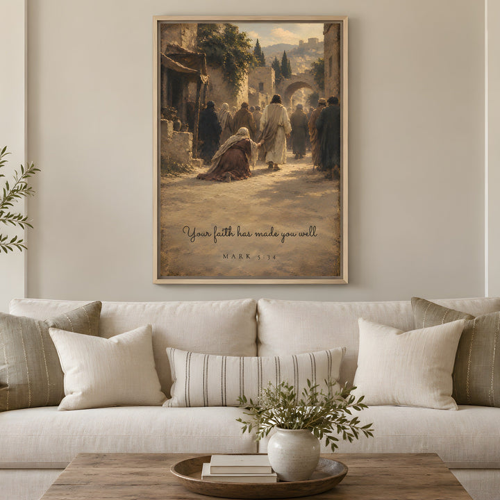 A framed vertical art print depicting a biblical scene with figures and the quote 'Your faith has made you weak' from Mark 11:24, displayed on a beige wall above a white sofa in a styled living room.