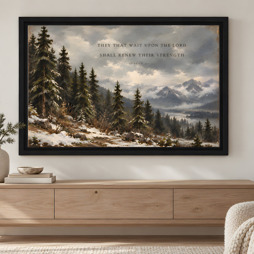 A framed landscape art print featuring a snowy pine forest and mountains with a Bible verse, displayed on a light gray wall above a wooden console table in a styled living room.