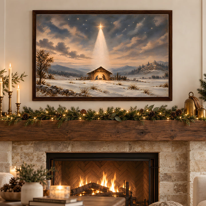 A framed Christmas landscape painting hangs above a stone fireplace in a cozy living room. The painting depicts a snowy winter scene with a small stable under a glowing star in the night sky.