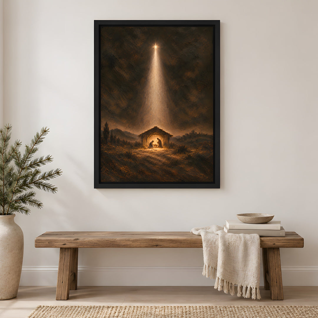 A framed vertical art print depicting a nativity scene with a bright beam of light shining down into a stable, hung on a white wall in a styled living room setting above a wooden bench.