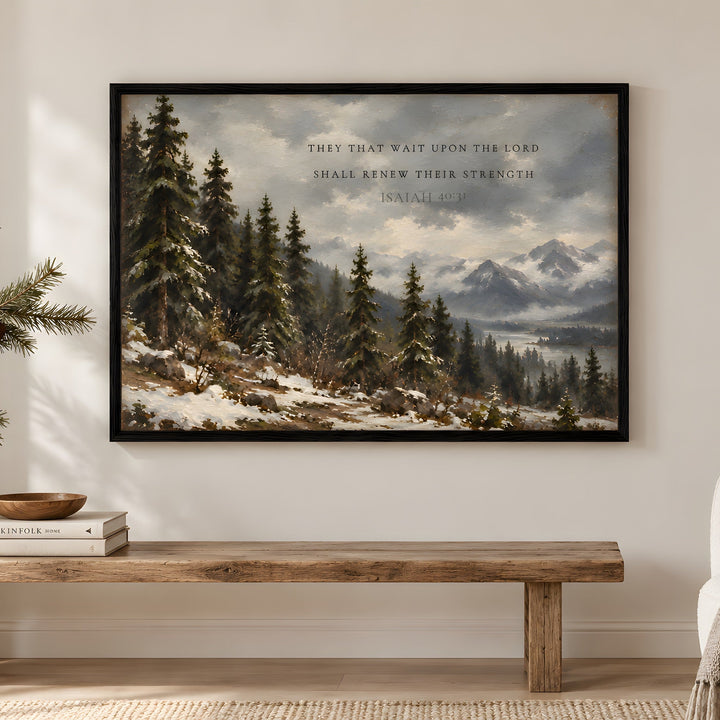 A framed winter landscape art print hangs on a white wall above a cream bouclé armchair in a styled living room. The artwork depicts snow-covered pine trees, distant mountains, and a cloudy sky with the text, 'THEY THAT WAIT UPON THE LORD SHALL RENEW THEIR STRENGTH - SAMUEL II: 15.