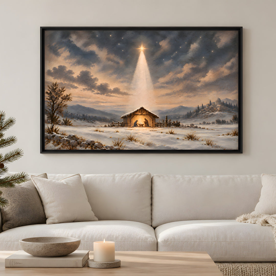 A framed Christmas landscape painting hangs above a stone fireplace in a cozy living room. The painting depicts a snowy winter scene with a small stable under a glowing star in the night sky.