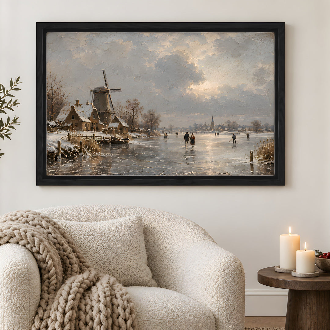 A framed winter landscape painting hangs on a white wall above a cream bouclé armchair in a styled living room. The artwork depicts a snowy village with a windmill by a frozen river, people skating on the ice, and a cloudy sky.