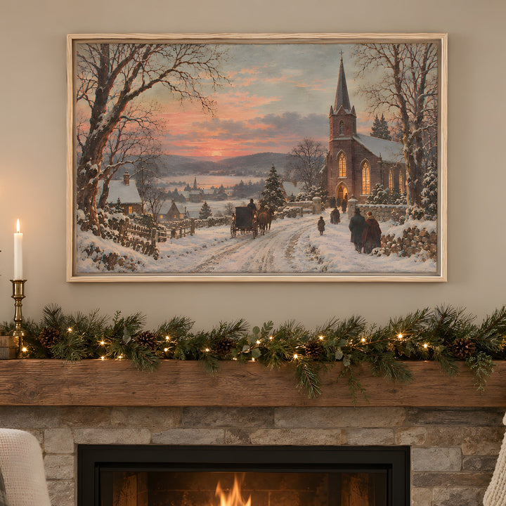 A framed winter landscape painting hangs above a stone fireplace mantel decorated with green garland, pinecones, candles, and stockings. The painting depicts a snowy village street with a church, bare trees, and a warm sunset sky.