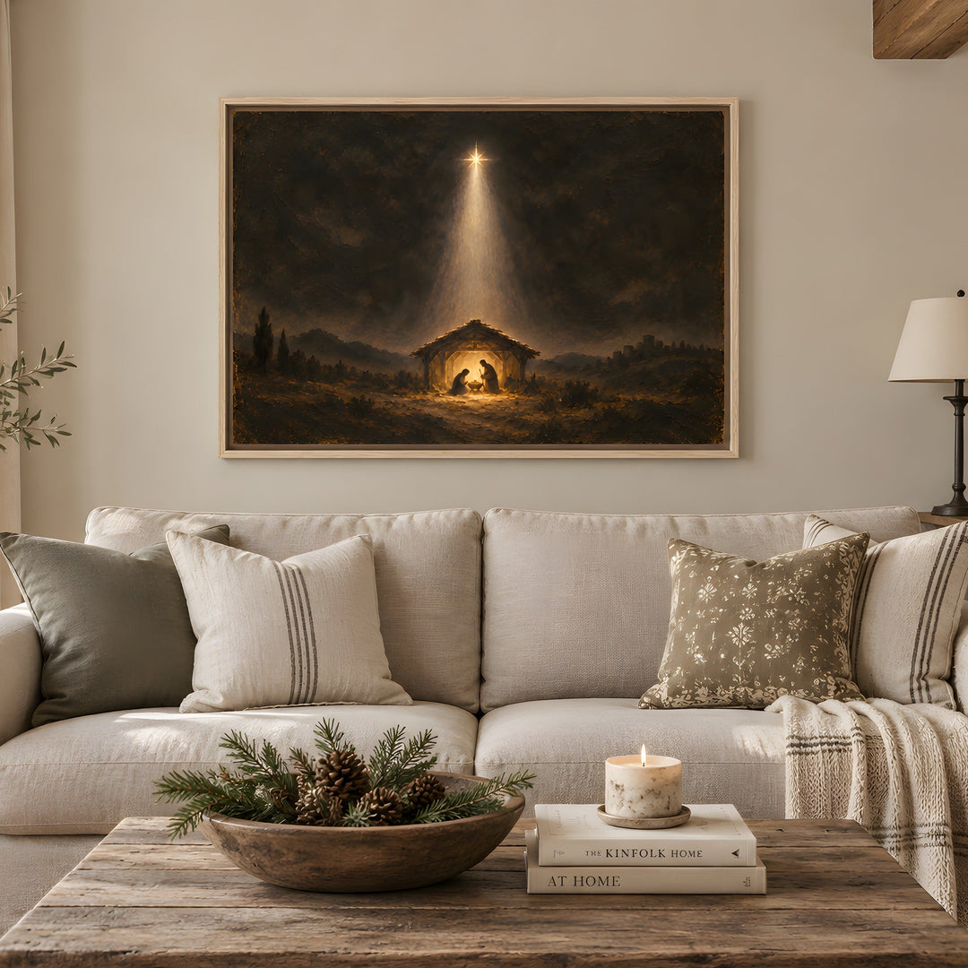 A large framed art print depicting a Christmas nativity scene with a bright beam of light, displayed on a beige wall above a light-colored sofa in a styled living room.