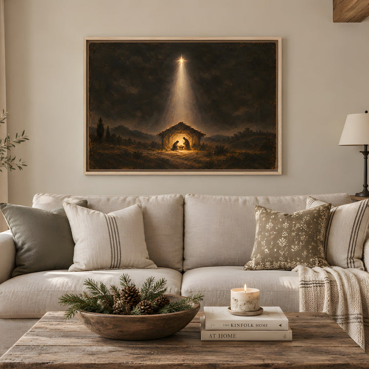 A large framed art print depicting a Christmas nativity scene with a bright beam of light, displayed on a beige wall above a light-colored sofa in a styled living room.