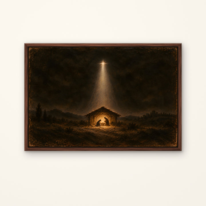 A framed dark religious painting depicting a stable at night with a bright star shining down, shown against a plain off-white wall.