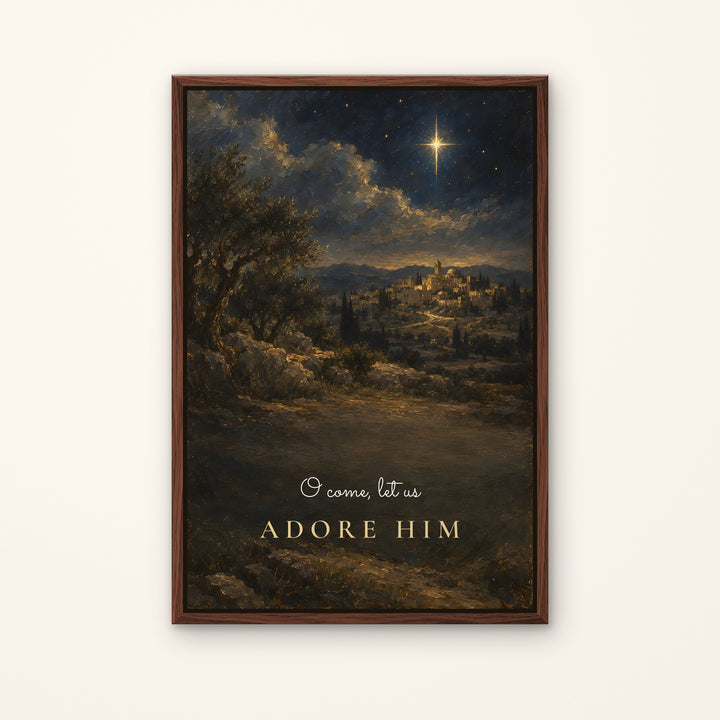 A framed vertical art print depicting a night landscape with a glowing star over a hillside town, with the text 'I come, let us ADORE HIM' in gold at the bottom, shown against a light beige wall.