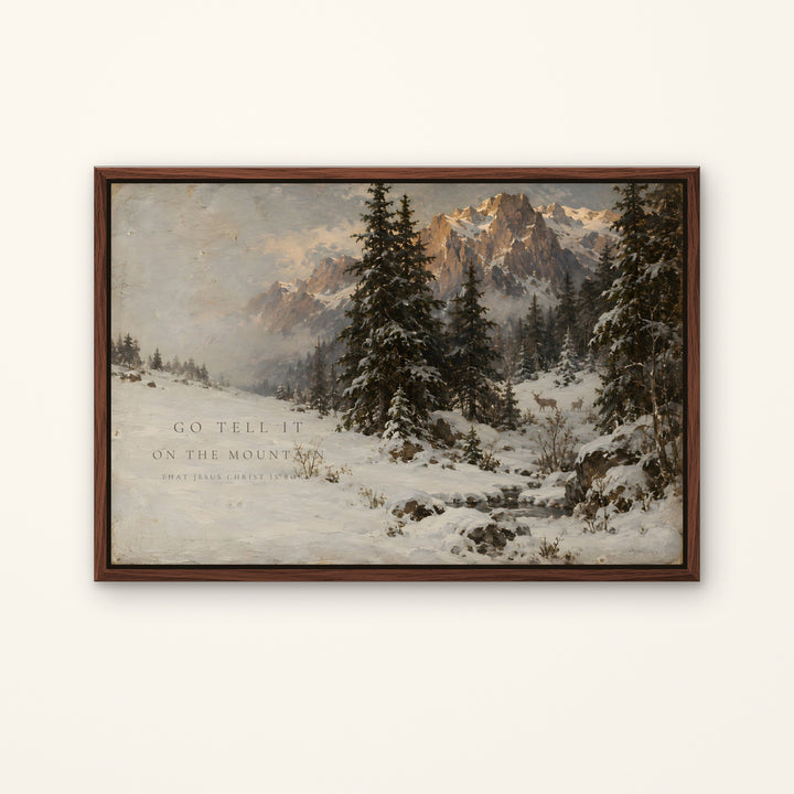 A framed landscape painting of a snowy mountain scene with pine trees, shown hanging on a light beige wall. The artwork includes the text 'GO TELL IT ON THE MOUNTAIN' and a smaller quote below.